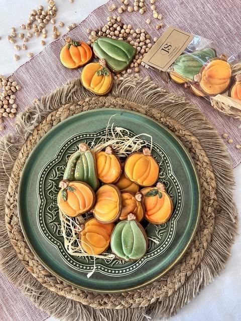 Styled autumn flat lay with decorative green plate containing small pumpkin and gourd decorations surrounded by scattered chickpeas and harvest items on purple fabric