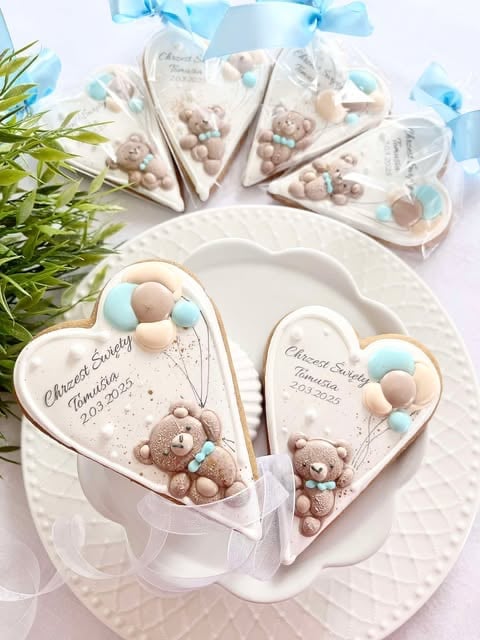 Heart-shaped white favors with teddy bears and blue accents arranged on a plate with green florals for a baby shower