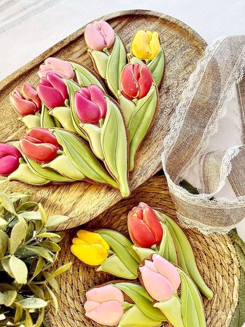 Colorful tulips in pink, red, and yellow arranged in woven baskets with green leaves on a wooden surface